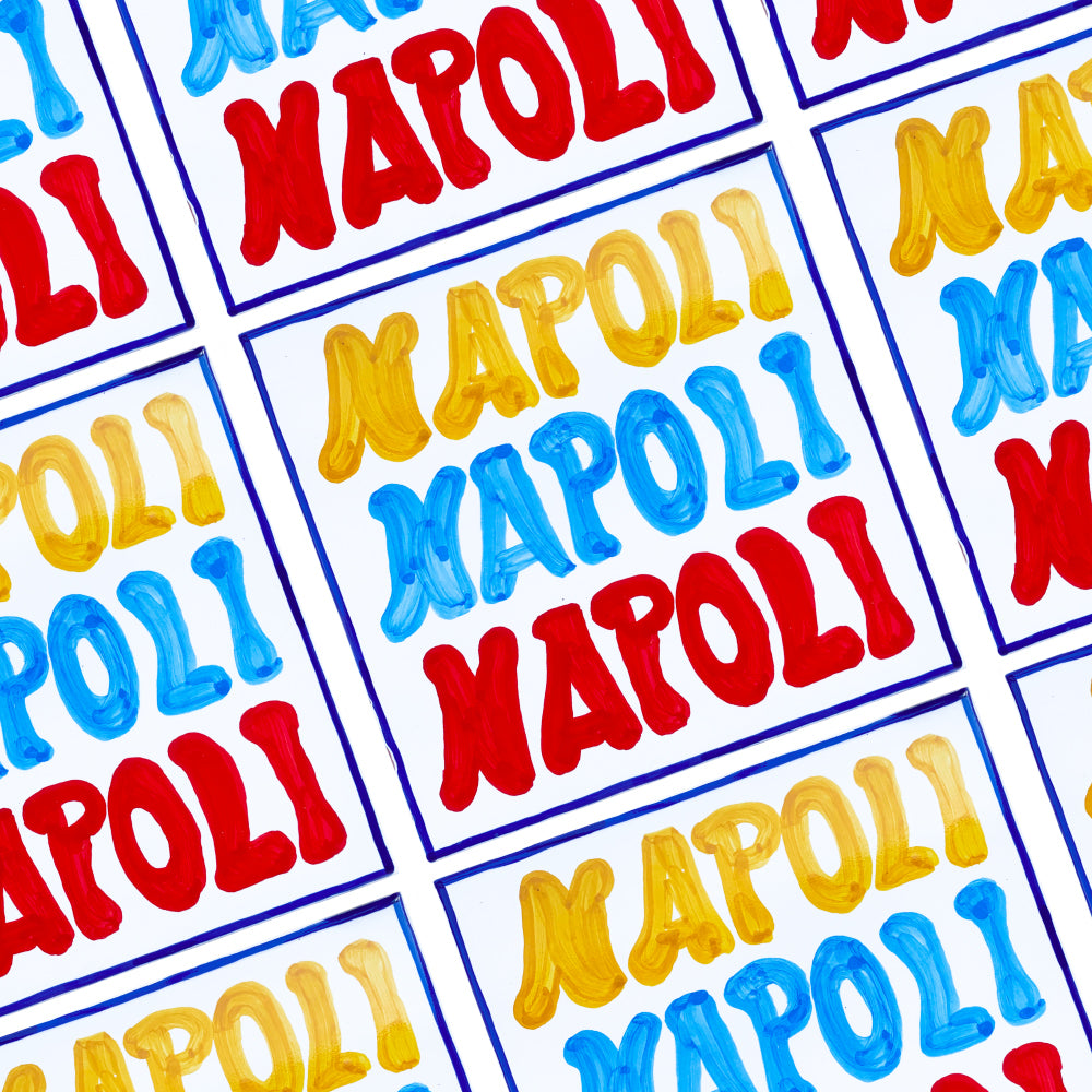 Maiolica artigianale in terracotta rossa smaltata, decorata a mano con la scritta “Napoli” in vivaci tonalità giallo, azzurro e rosso. Un omaggio colorato e autentico alla tradizione ceramica napoletana.