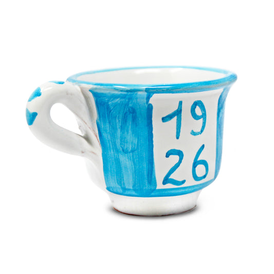 Può includere: Una tazza da tè in ceramica blu e bianca con i numeri "1926" dipinti sopra. I numeri sono visualizzati anche in un carattere più grande sopra la tazza. La tazza ha un manico bianco e un design dipinto.