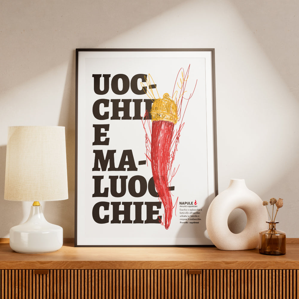 Il poster raffigura un grande corno portafortuna napoletano di colore rosso, sormontato da una corona dorata, disegnato con tratti grafici stilizzati. Sullo sfondo, in caratteri neri e grandi, appare la scritta dialettale Uocchie e Maluocchie. In basso a destra e presente un testo esplicativo che richiama un proverbio napoletano legato alla tradizione degli amuleti contro il malocchio