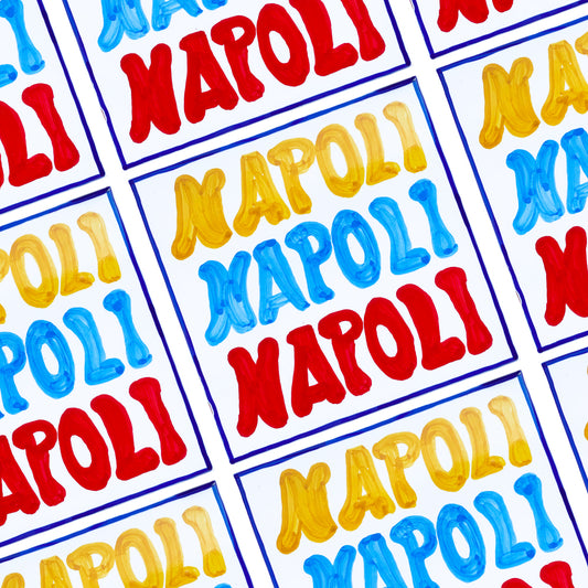 Maiolica artigianale in terracotta rossa smaltata, decorata a mano con la scritta “Napoli” in vivaci tonalità giallo, azzurro e rosso. Un omaggio colorato e autentico alla tradizione ceramica napoletana.