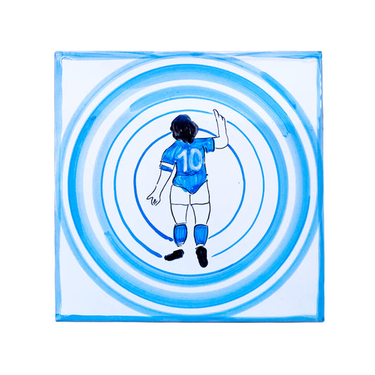 Maiolica Pil Pil raffigurante Diego Armando Maradona di spalle con la maglia numero 10, immerso in cerchi concentrici azzurri su sfondo bianco, in stile pop iconico napoletano.