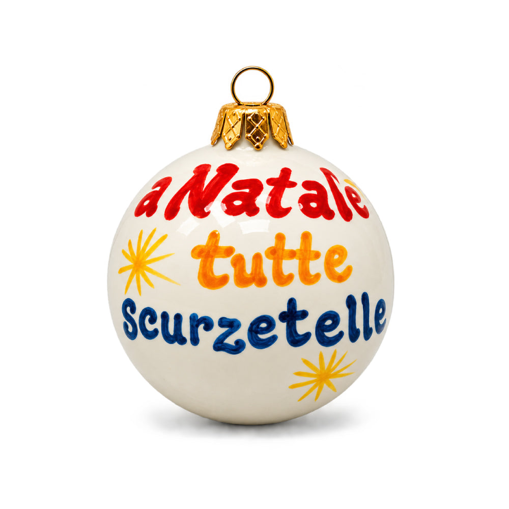 Palla di Natale napoletana artigianale Pil Pil, bianca e dipinta a mano, con scritta “A Natale tutte scurzetelle” in rosso, arancione e blu, stelle gialle e gancio dorato. Decorazione ispirata ai gusci della frutta secca sulle tavole natalizie di Napoli.