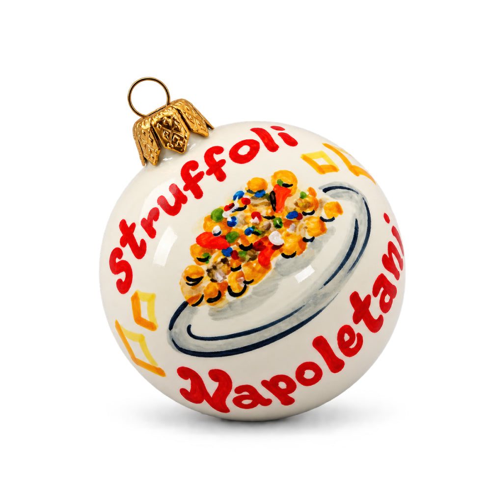 Palla di Natale artigianale Pil Pil Design Partenopeo, bianca e dipinta a mano, con illustrazione di un piatto di struffoli napoletani decorati con miele e confettini colorati. Scritta rossa “Struffoli Napoletani”, dettagli gialli e gancio dorato. Addobbo natalizio ispirato alla tradizione gastronomica di Napoli.