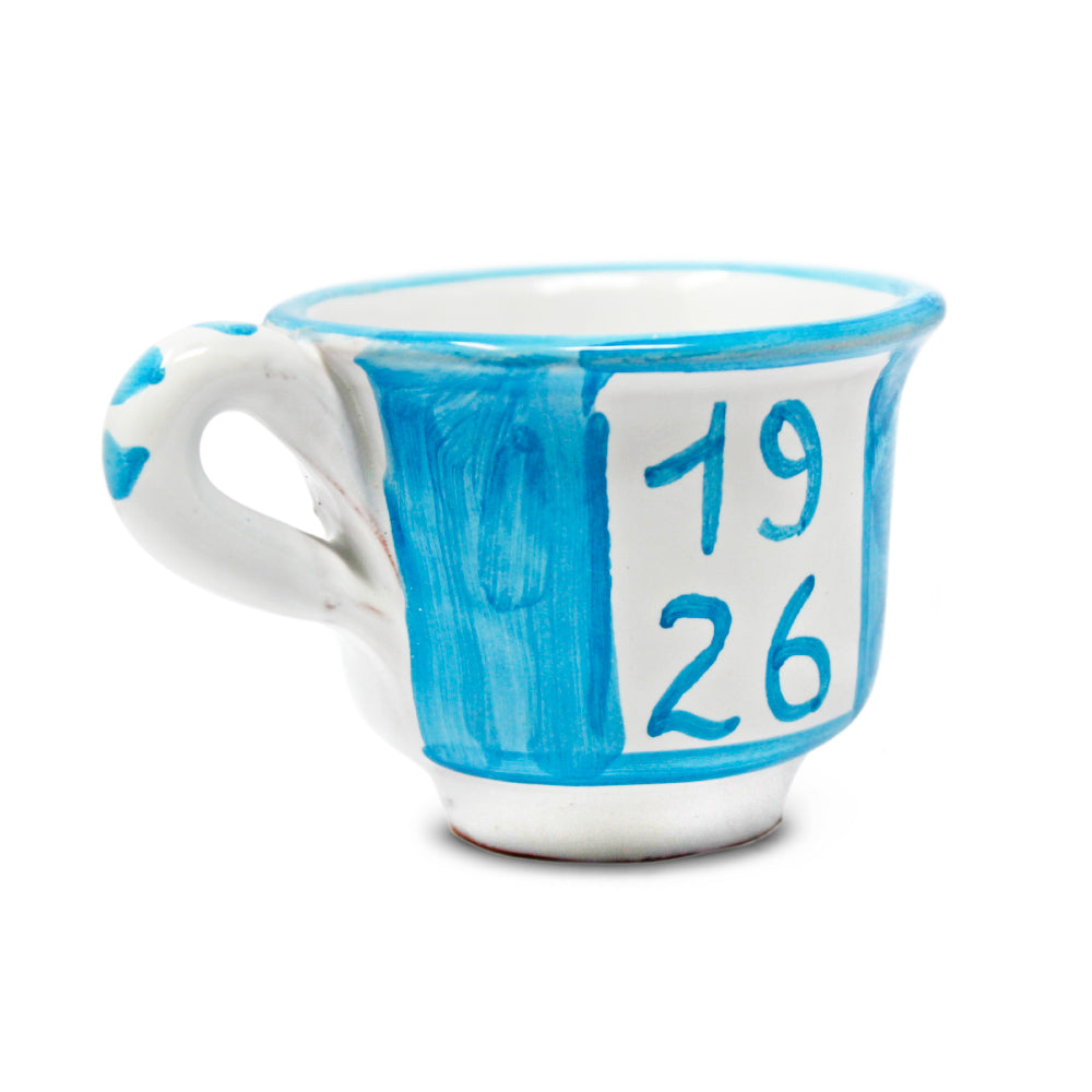 Può includere: Una tazza da tè in ceramica blu e bianca con i numeri "1926" dipinti sopra. I numeri sono visualizzati anche in un carattere più grande sopra la tazza. La tazza ha un manico bianco e un design dipinto.