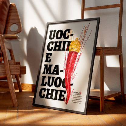Il poster raffigura un grande corno portafortuna napoletano di colore rosso, sormontato da una corona dorata, disegnato con tratti grafici stilizzati. Sullo sfondo, in caratteri neri e grandi, appare la scritta dialettale Uocchie e Maluocchie. In basso a destra e presente un testo esplicativo che richiama un proverbio napoletano legato alla tradizione degli amuleti contro il malocchio